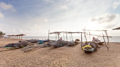 Una playa con cabañas de techo de paja, barcos y un mar tranquilo.