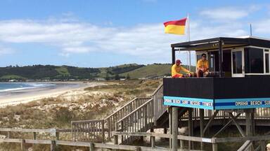 A lifeguard tower at Omaha Beach with a flag, beach, and hills in the background.