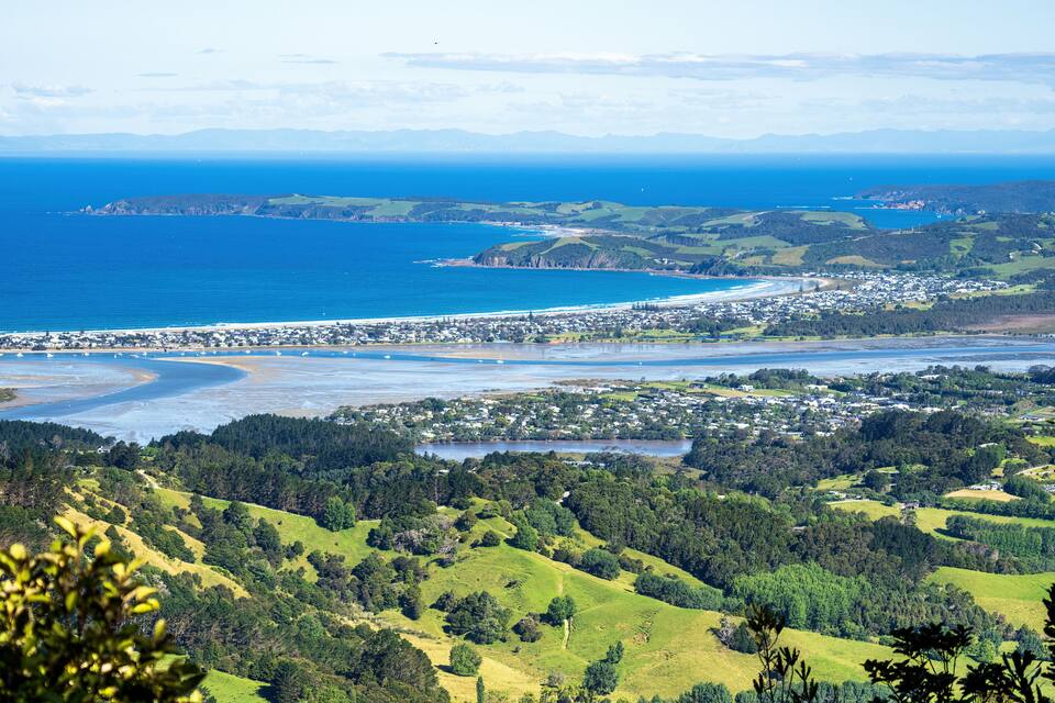 A coastal town with a beach, green hills, and a clear blue sea.