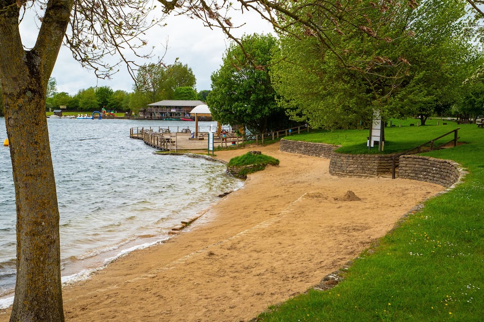 A sandy beach with a wooden pier, a gazebo, and a stone wall.