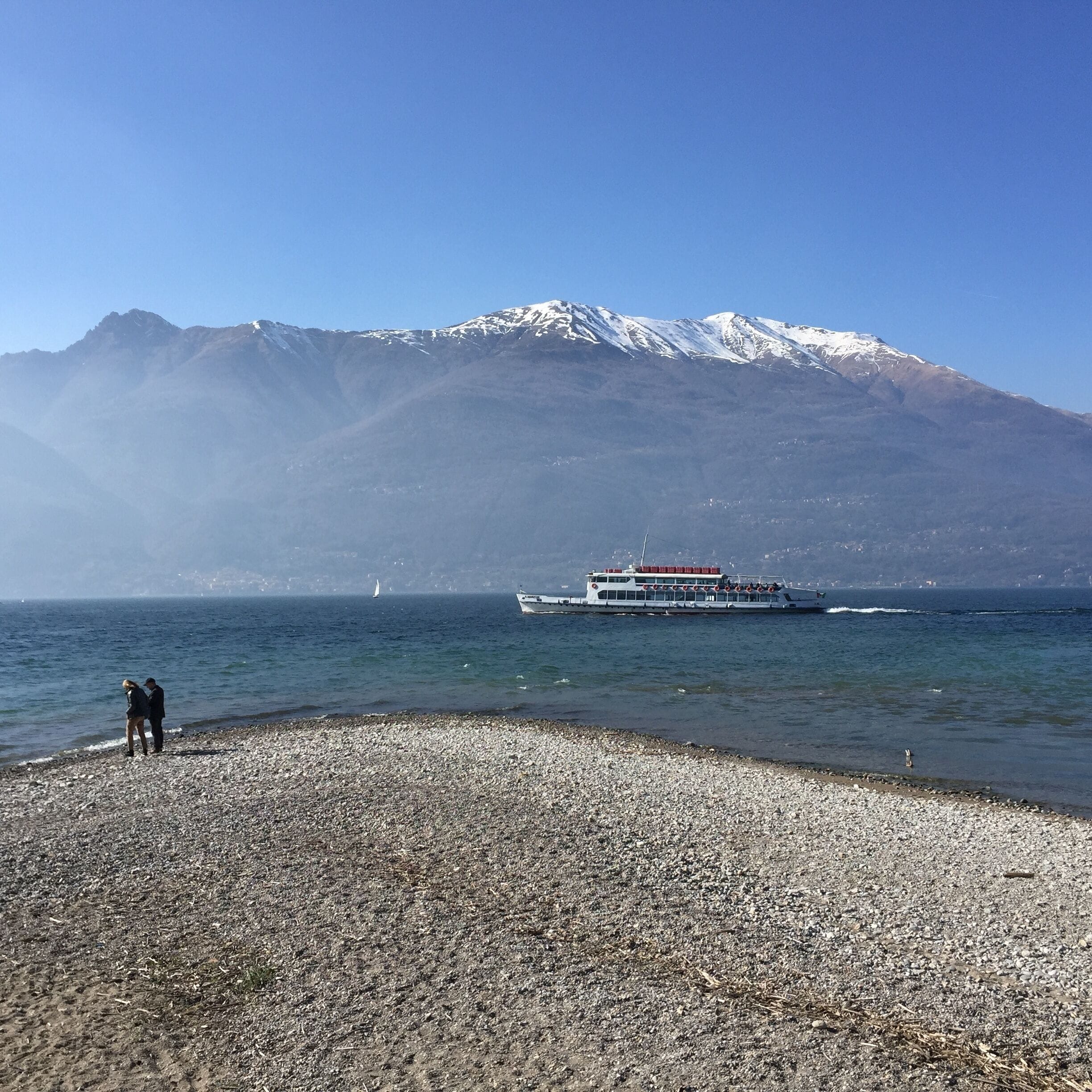 A rocky beach with a boat on the water and a mountain in the background.
