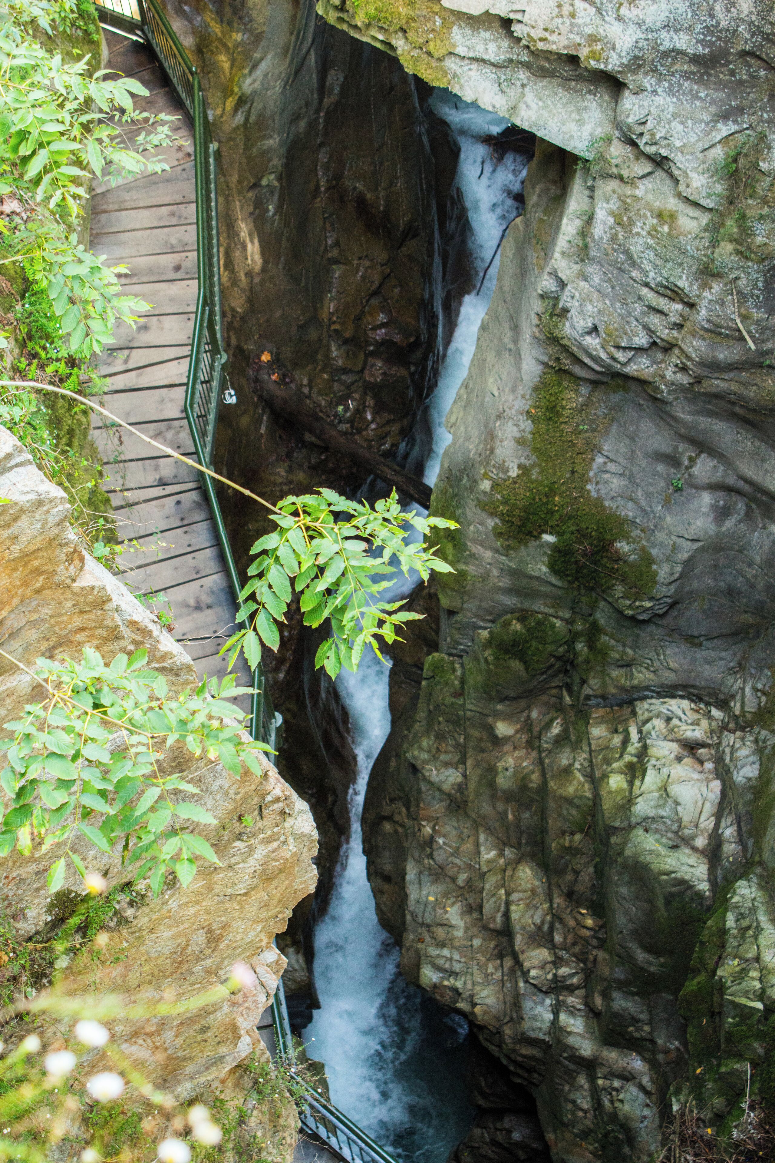 A waterfall cascading down a rocky cliff, surrounded by greenery and a wooden walkway.