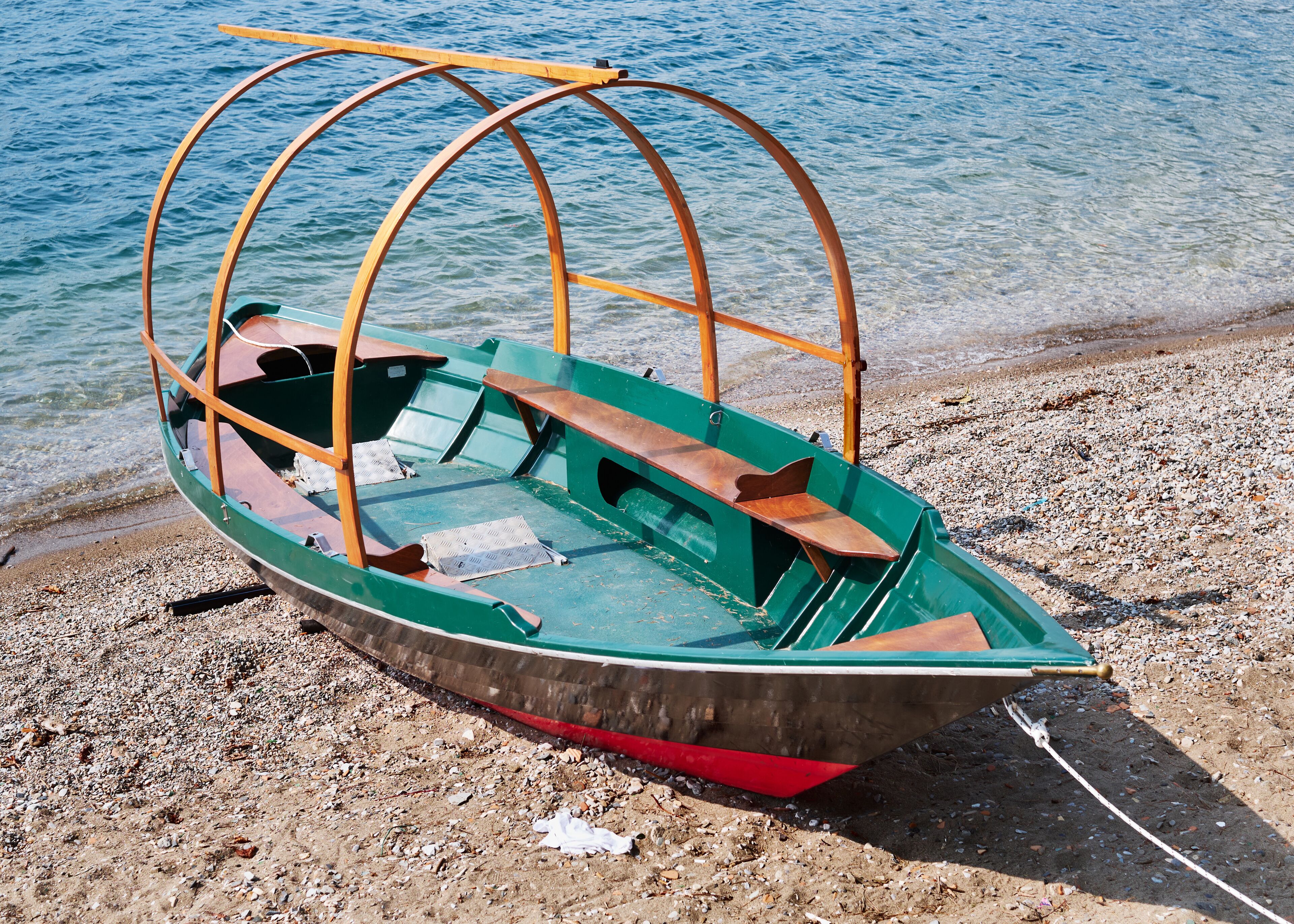 A green boat with a wooden structure on a pebbly beach by the water.