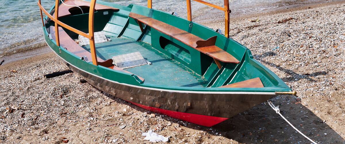 A green boat with a wooden structure on a pebbly beach by the water.