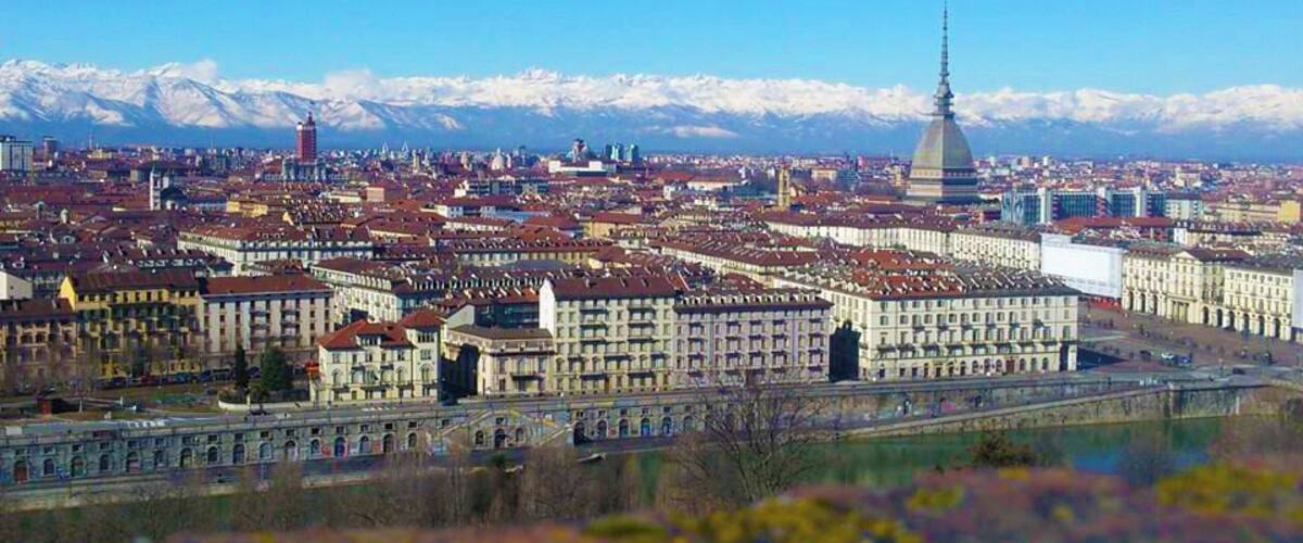 A cityscape with a prominent tower and snow-capped mountains in the background.