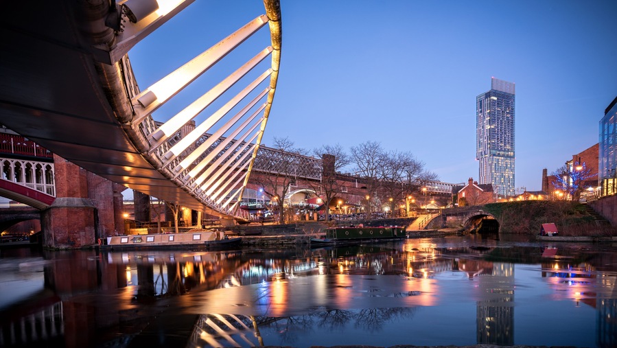 A modern bridge with cables, a river, and a tall building in the background.