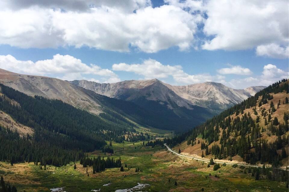 A mountainous landscape with a winding road, green valleys, and dense forests.