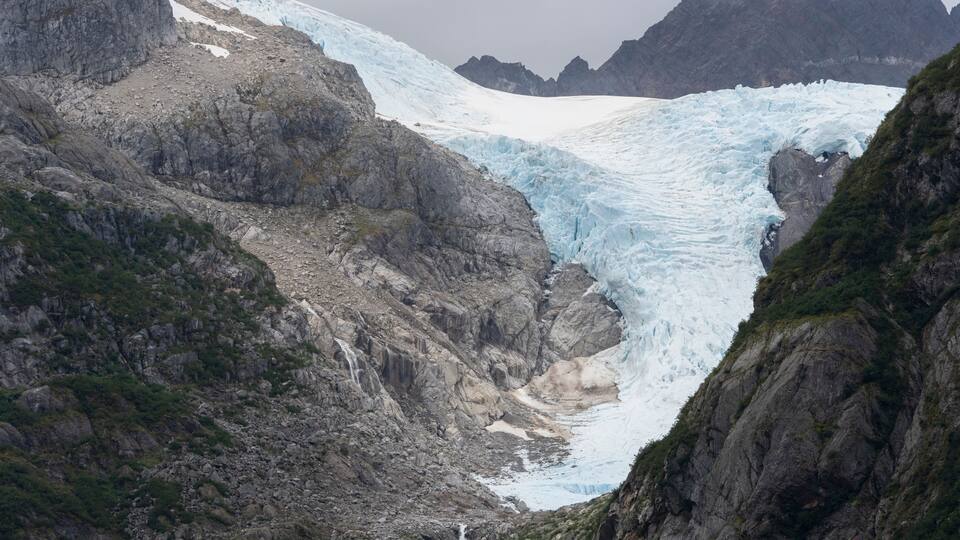 A glacier with a waterfall, rocky terrain, and mountains in the background.