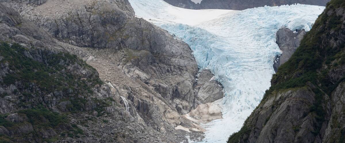 A glacier with a waterfall, rocky terrain, and mountains in the background.