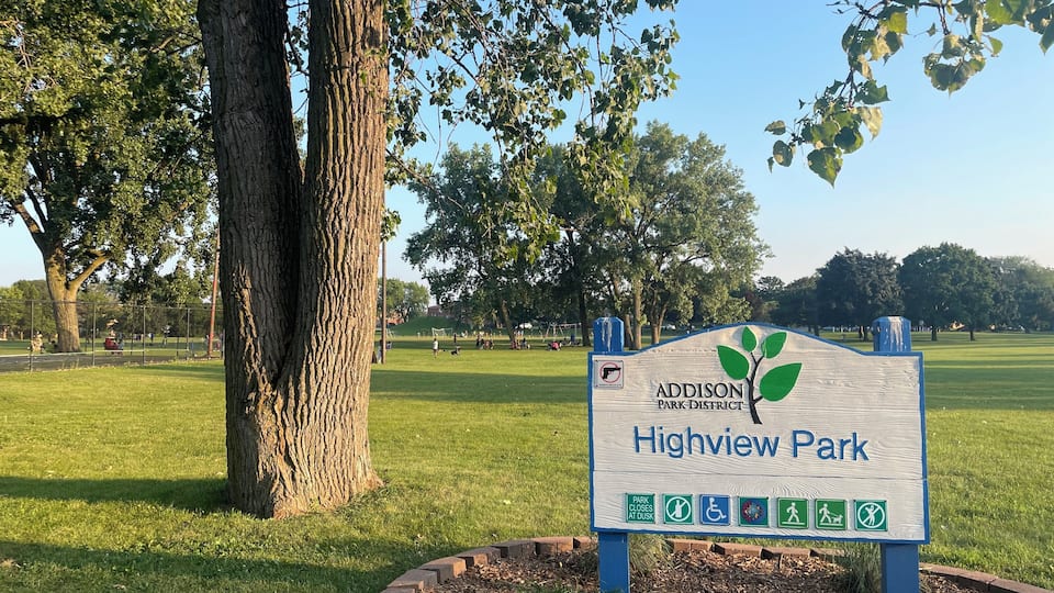 A park sign for Addison Park District Highview Park with a tree and grass in the background.