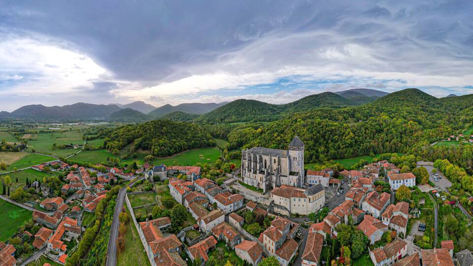 A historic town with a prominent church, surrounded by lush green hills and a river.