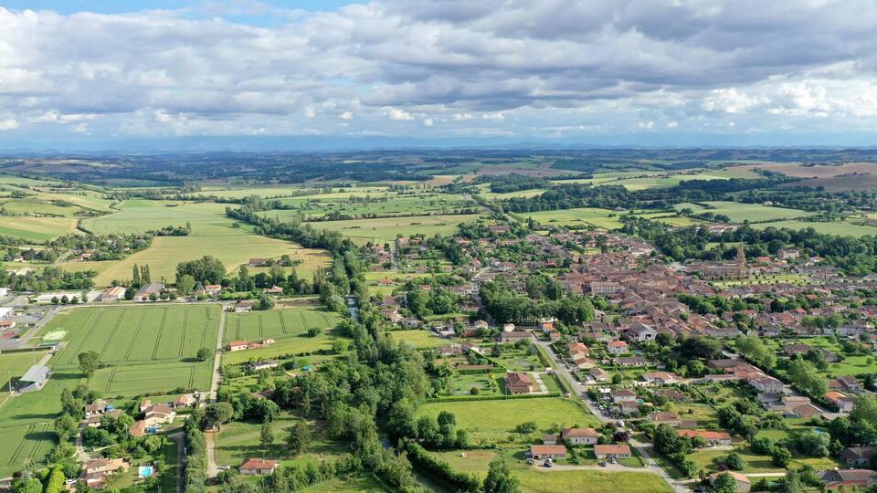 A rural landscape with fields, a small town, and distant mountains.