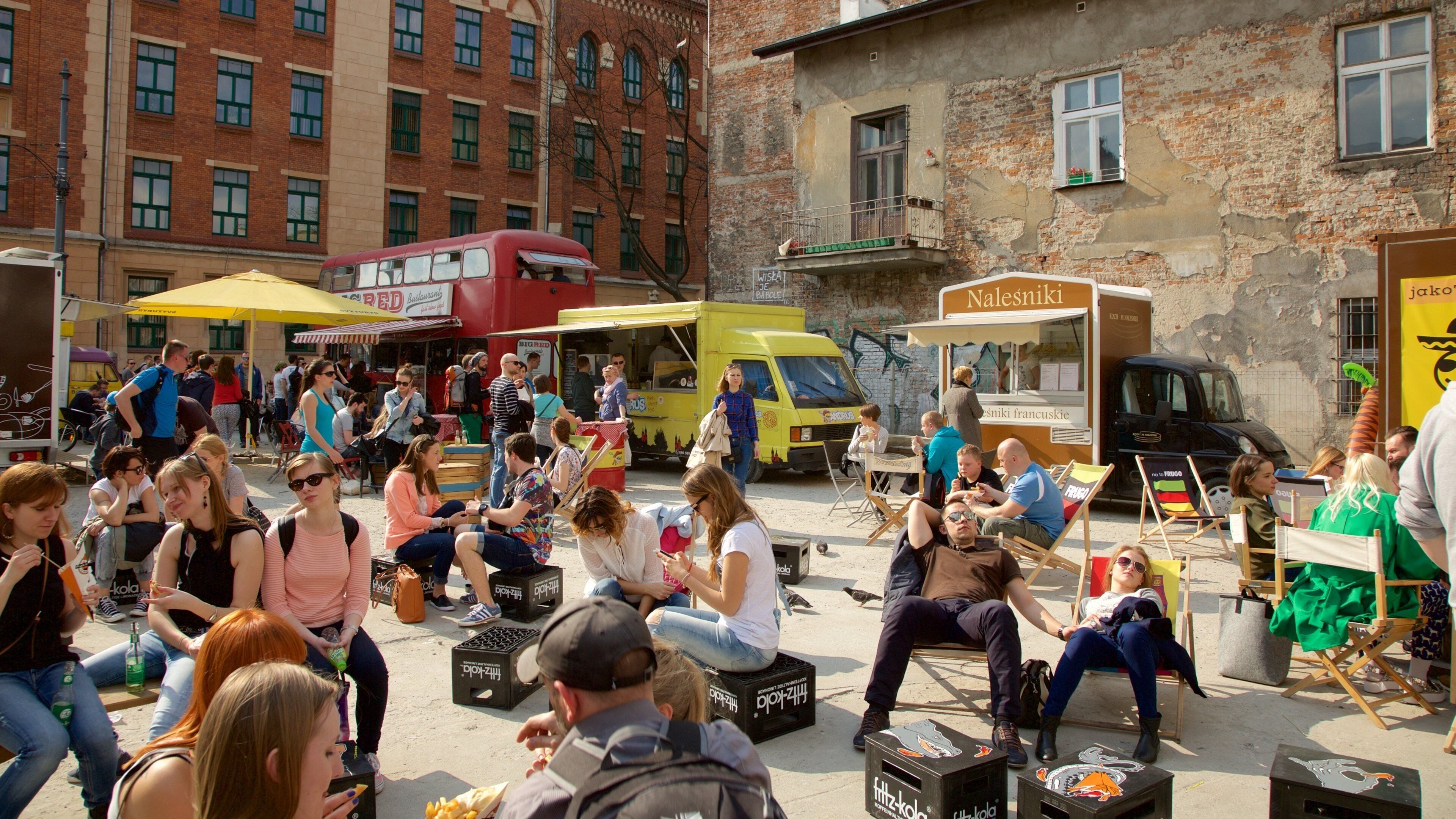 Mercado al aire libre con puestos de comida y gente sentada en cajas.