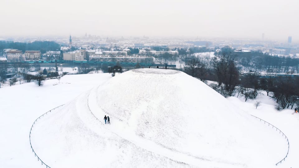 Panoramic view of the Krakus Mound (Kopiec Krakusa) also called Krak Mound. A tumulus located in the Podgórze district of Kraków, Poland. Tourists can be seen standing. Whole area covered with snow.