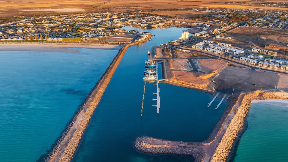 Vue aérienne d’une ville côtière avec un port de plaisance, un phare et une vaste étendue d’eau.