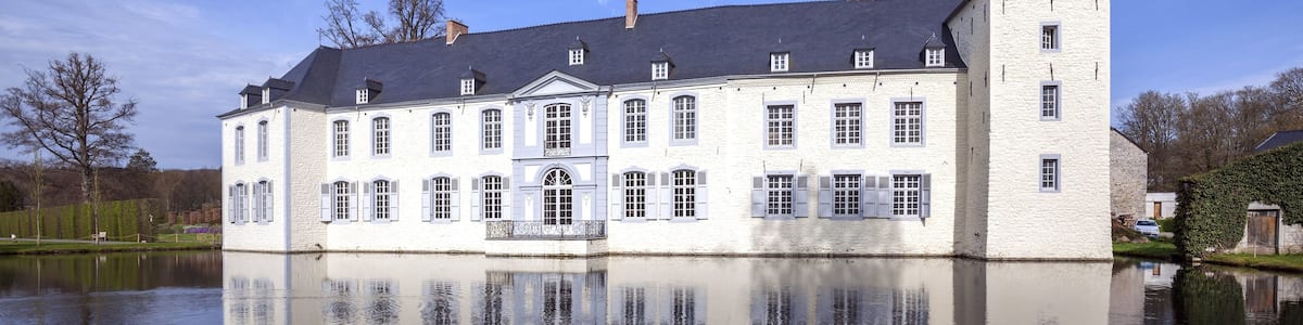 A large white building with a tower, reflecting on a calm body of water.