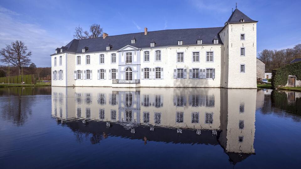 A large white building with a tower, reflecting on a calm body of water.