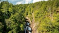 Ein bewaldetes Tal mit einem Wasserfall, der über eine felsige Klippe stürzt.