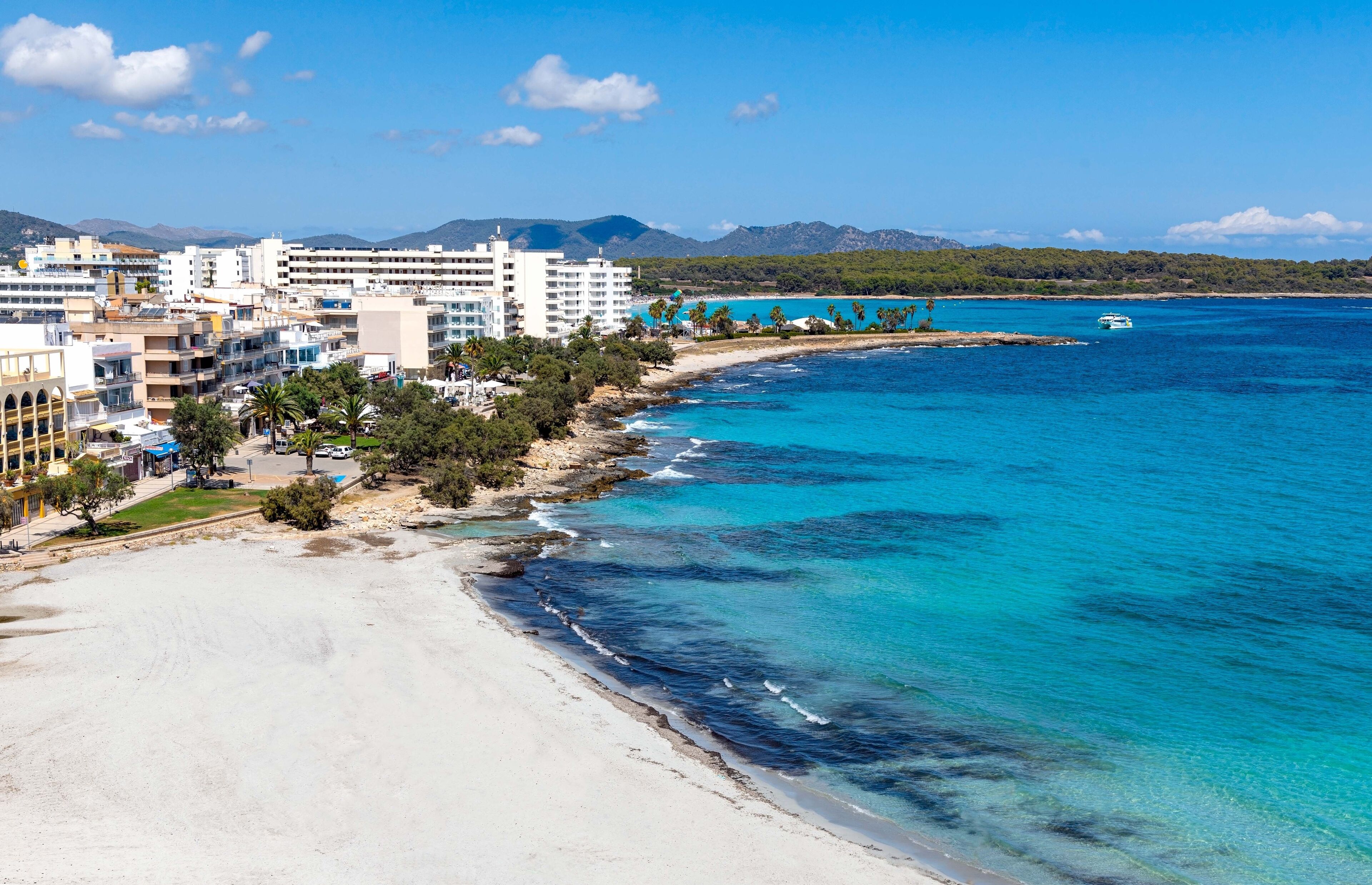 A coastal city with a beach, clear blue waters, and mountains in the background.