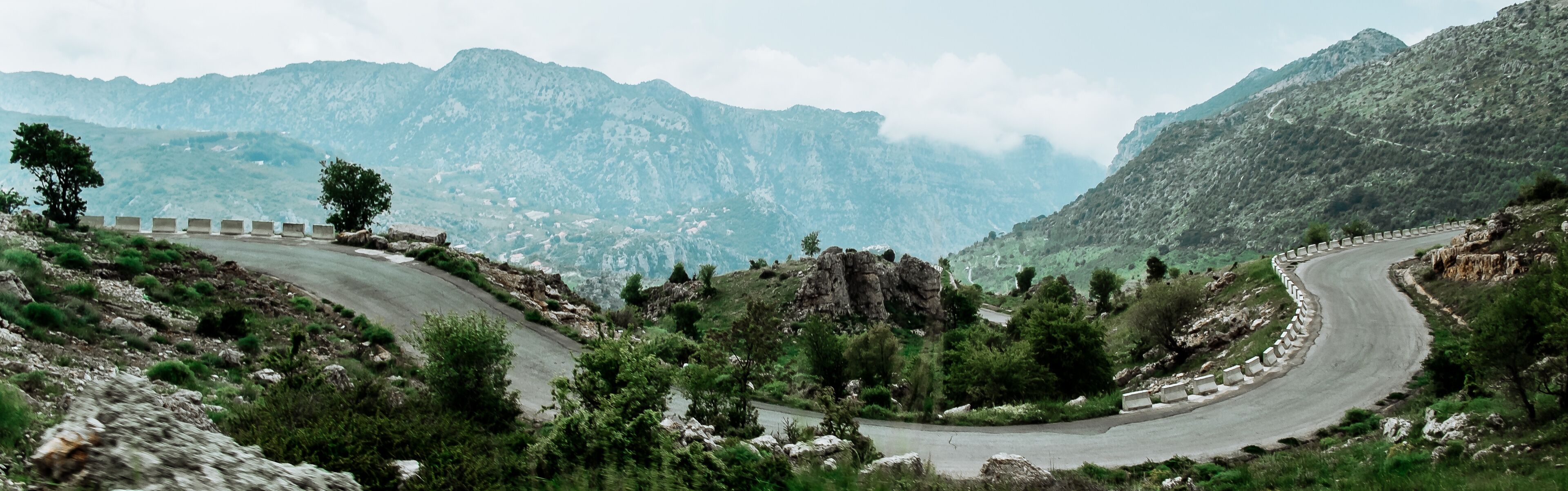 A winding mountain road with guardrails, surrounded by rocky terrain and sparse vegetation.