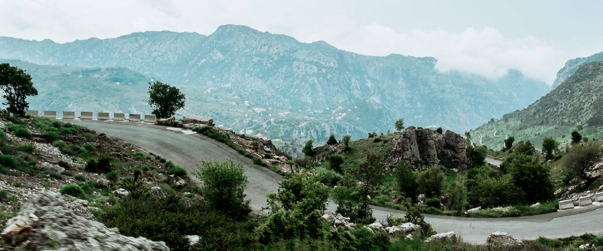 A winding mountain road with guardrails, surrounded by rocky terrain and sparse vegetation.