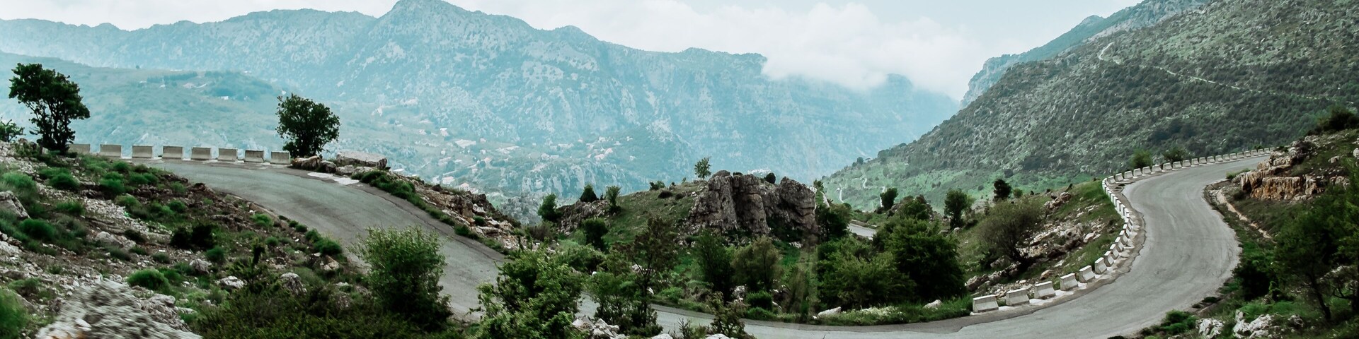 A winding mountain road with guardrails, surrounded by rocky terrain and sparse vegetation.