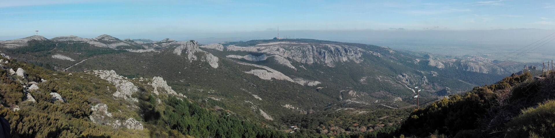 A mountainous landscape with rocky terrain, dense forests, and distant power lines.