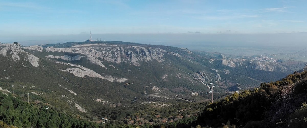 A mountainous landscape with rocky terrain, dense forests, and distant power lines.