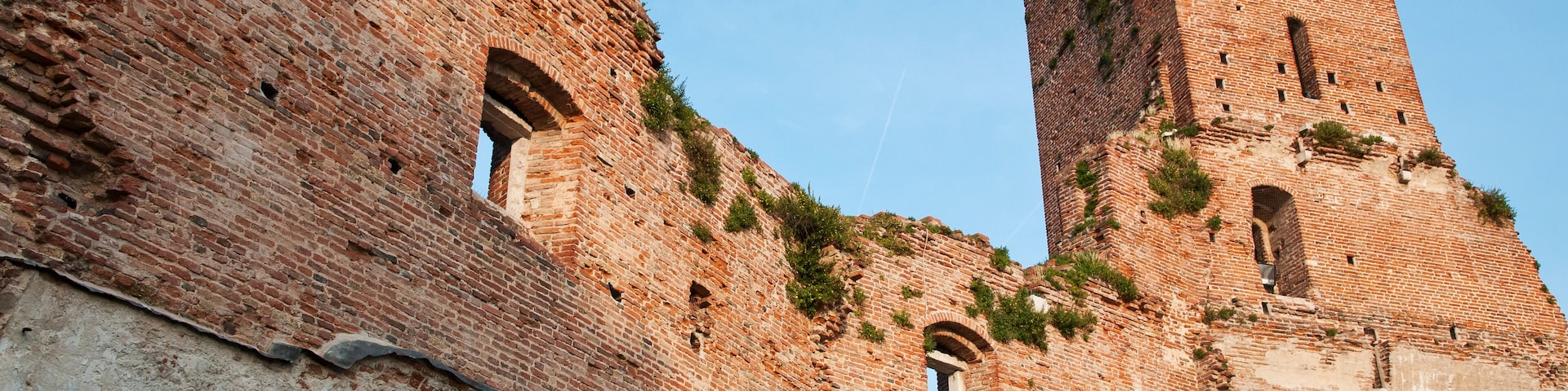 Una torre de ladrillo histórico con ventanas arqueadas y un gran muro con grafitis.