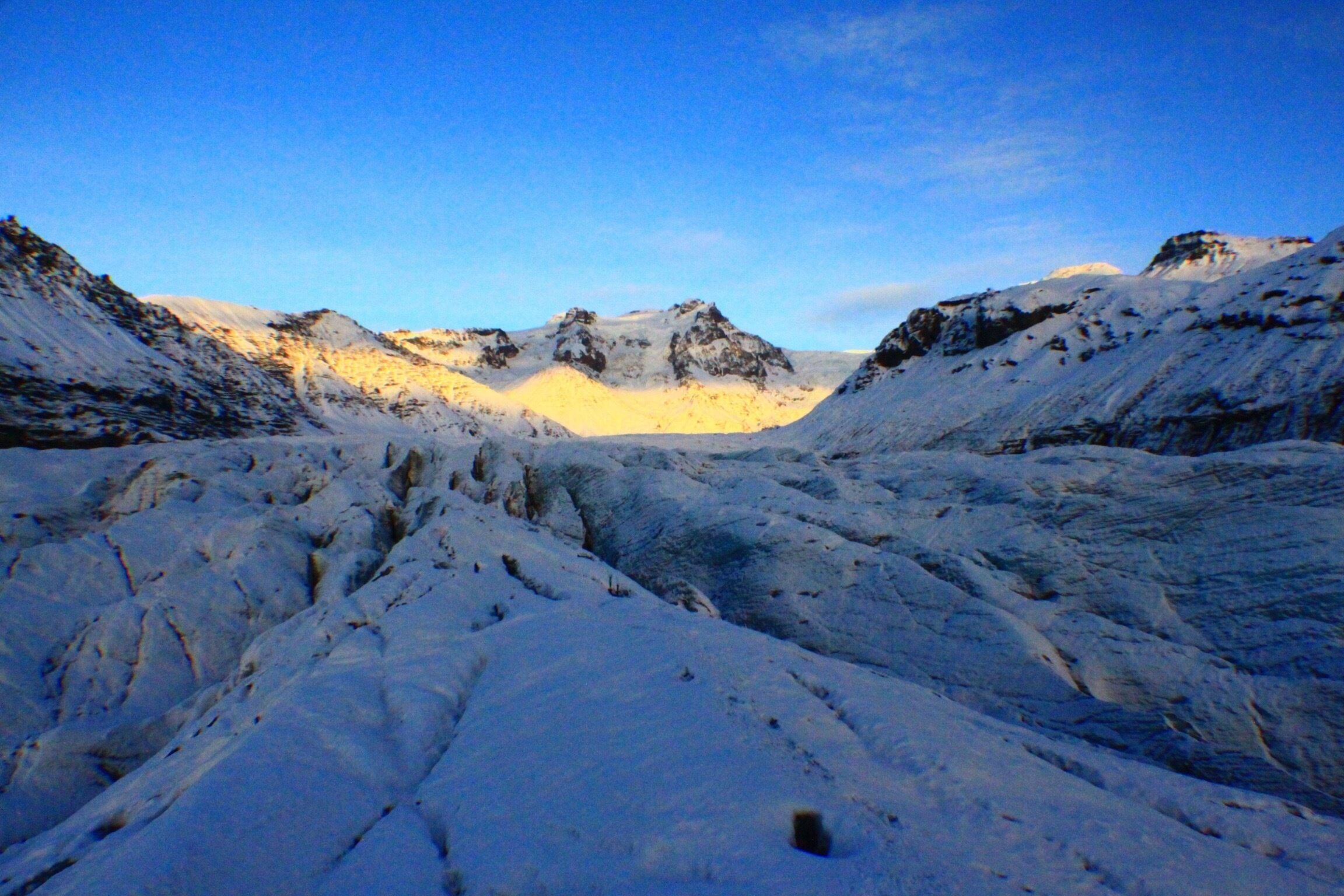 A snow-covered mountainous landscape with rugged terrain and rocky peaks under a clear blue sky.
