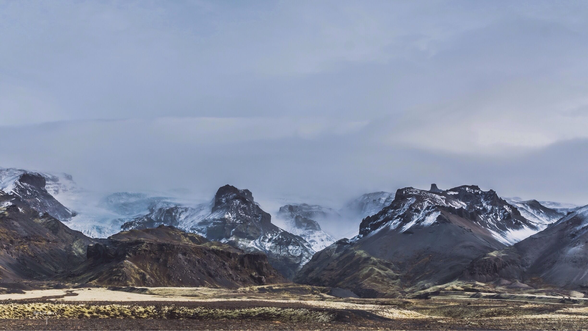 A rugged mountainous landscape with snow-capped peaks and a valley.