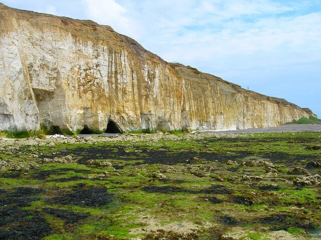 A coastal cliff with visible erosion patterns and a road running parallel to it.