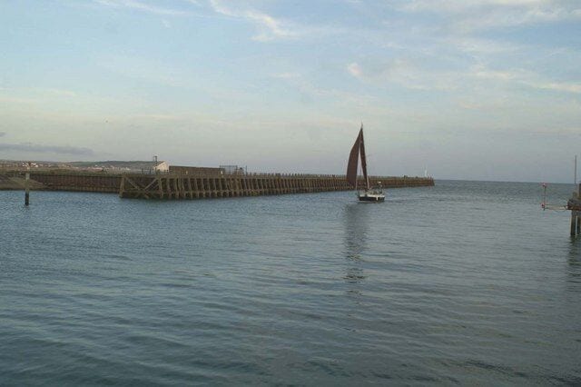 A pier extending into calm waters with a sailboat.