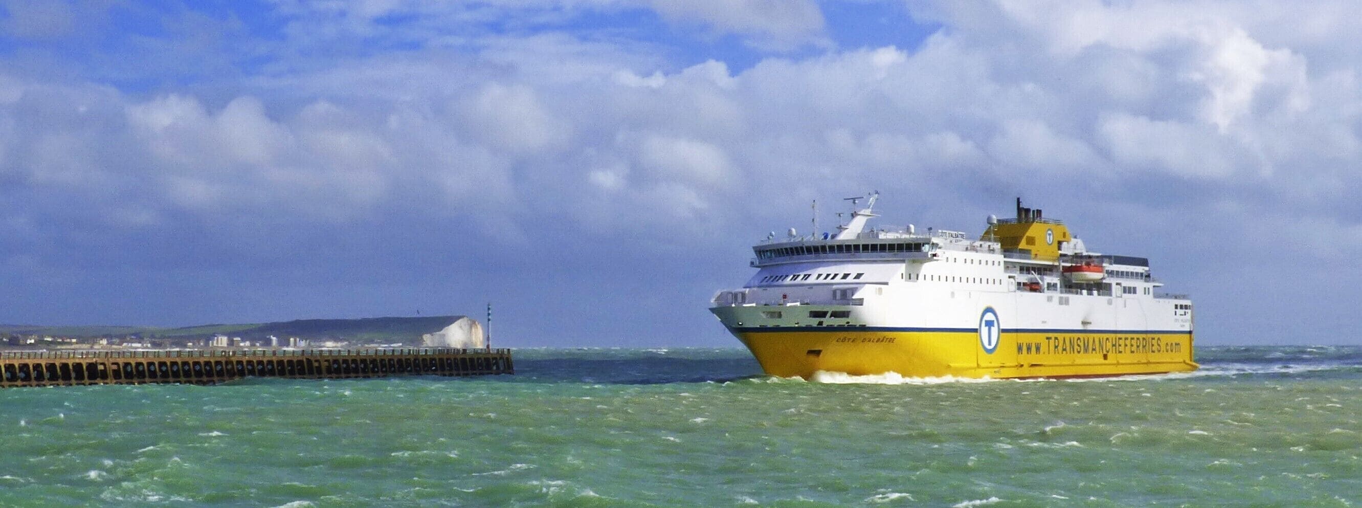 A large ferry with a yellow and white hull, navigating through choppy waters near a pier.