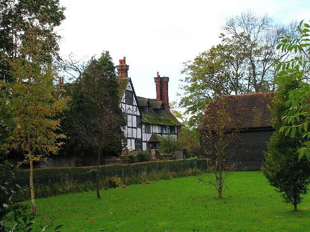 A Tudor-style house with a thatched roof, surrounded by a well-maintained garden and trees.