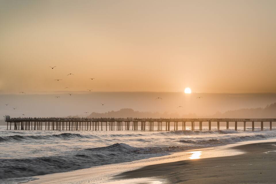 A pier extending into the ocean with waves crashing against it during sunset.