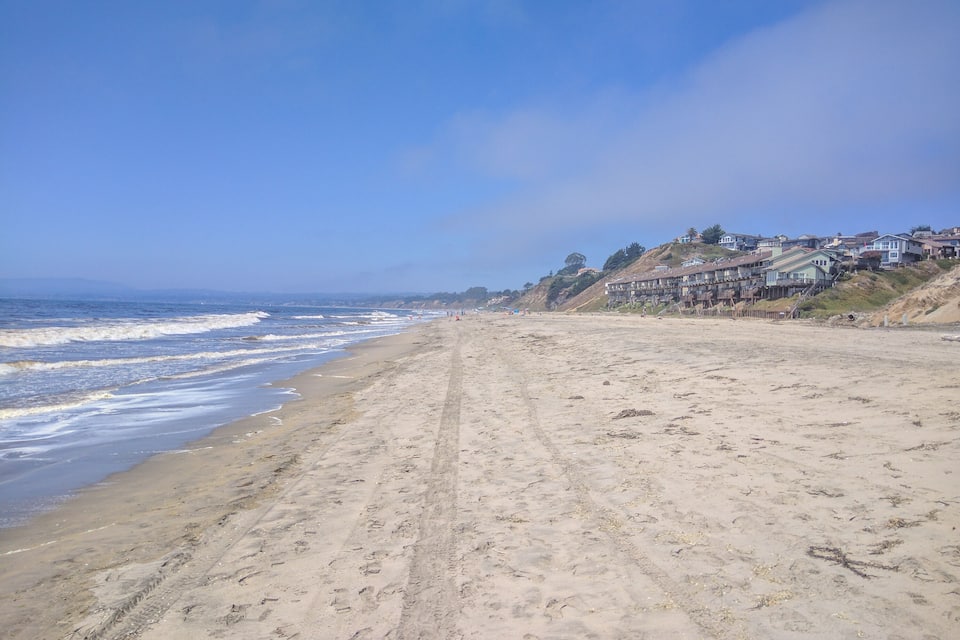 A sandy beach with waves, houses, and a clear sky.