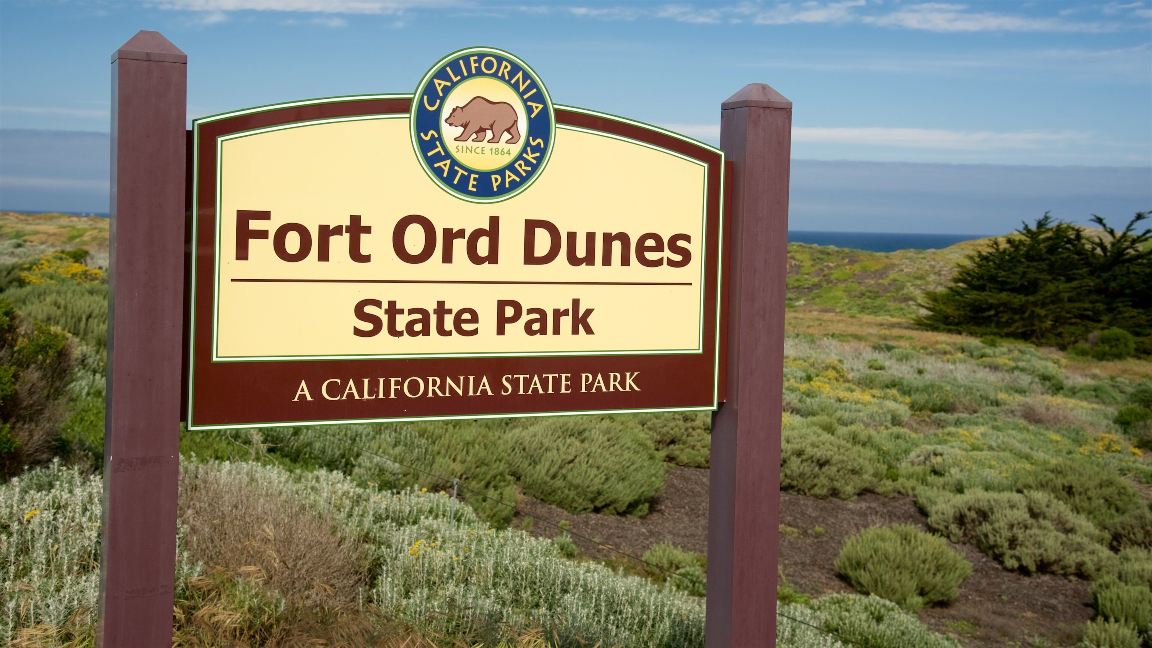 Segnaletica per il Fort Ord Dunes State Park, con un paesaggio costiero sullo sfondo.