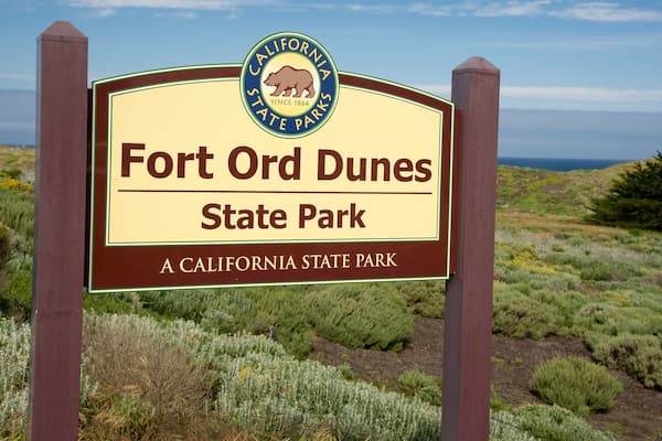 Schild für den Fort Ord Dunes State Park, im Hintergrund eine Küstenlandschaft.