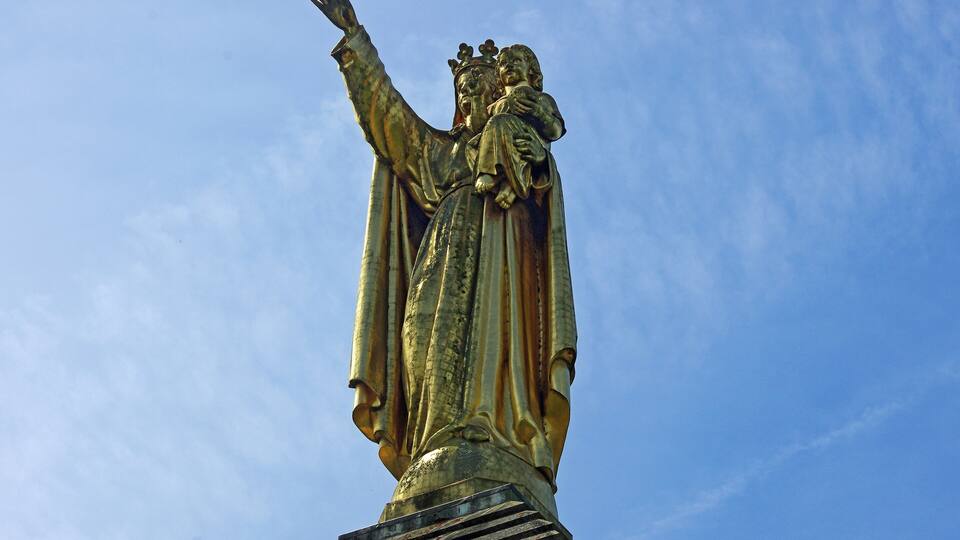 A statue of a robed figure with outstretched arms and a crown, set against a clear blue sky.