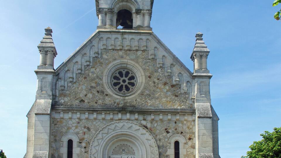 A historic church with a statue on top, a rose window, and a stone facade.