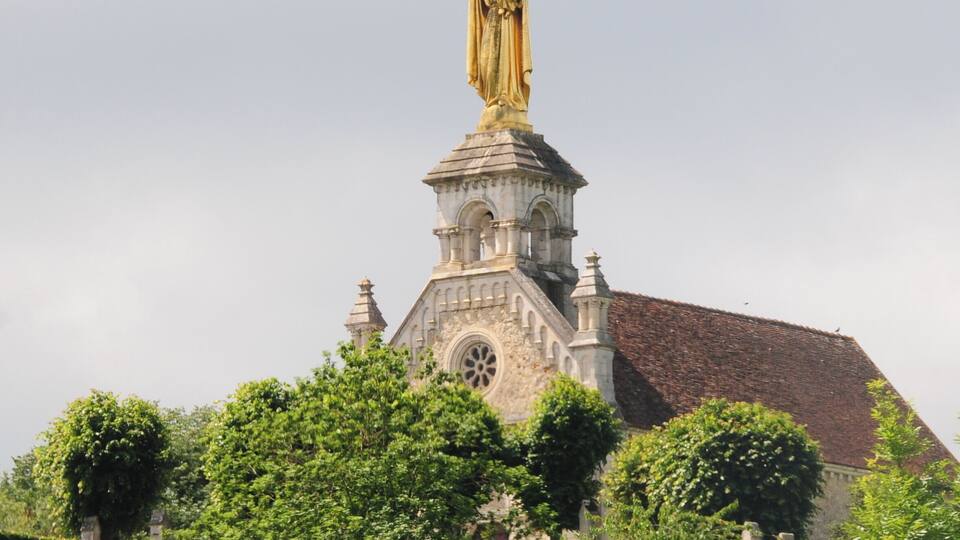 A church with a statue on top, surrounded by greenery.