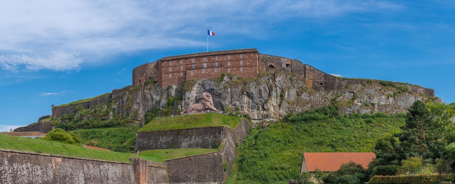 A historic fort with a lion statue, surrounded by lush greenery and a clear blue sky.