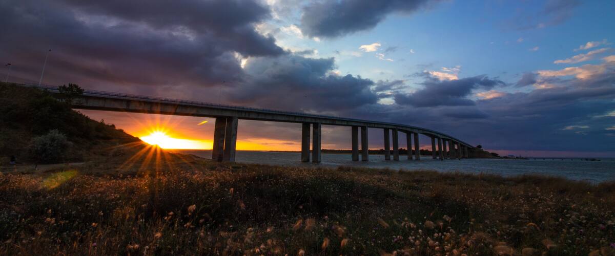 A bridge over water at sunset with a cloudy sky.