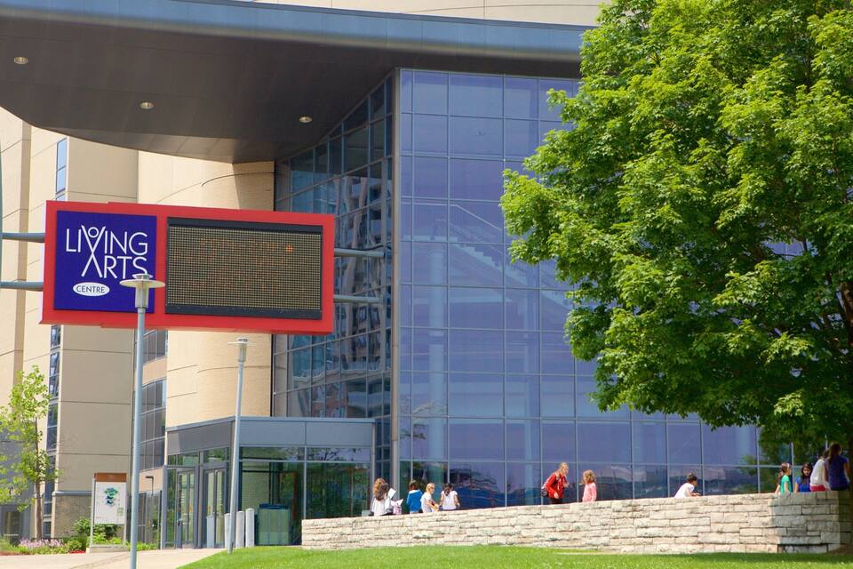 Un edificio moderno con una amplia fachada de vidrio, un cartel que indica el Living Arts Centre y una pared de piedra con gente sentada y caminando.