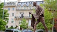 A statue of a man with a staff in front of a building with ornate architecture.