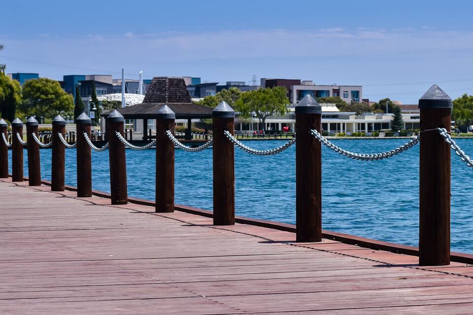 A wooden boardwalk with metal bollards and chains along a waterfront.