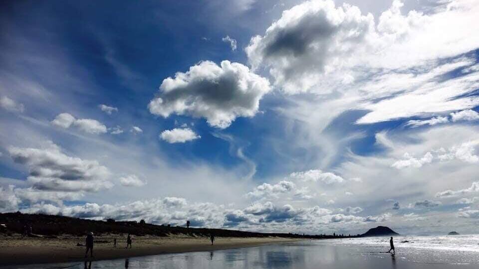 A beach with people walking, a clear sky with clouds, and a calm sea.