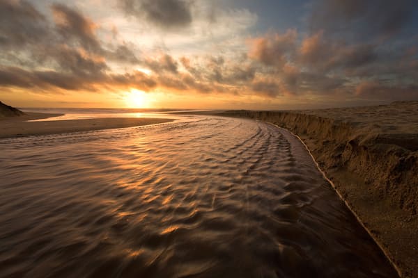 Una playa al atardecer con olas y un cielo nublado.