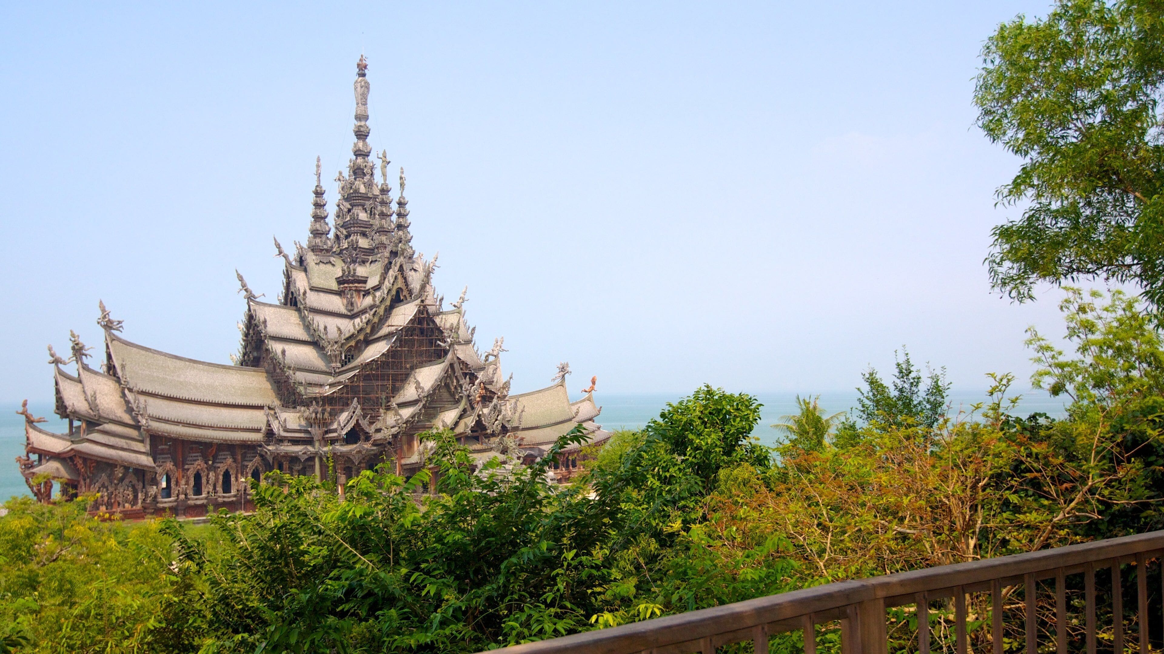 A traditional multi-tiered temple with ornate decorations, surrounded by lush greenery and overlooking a body of water.